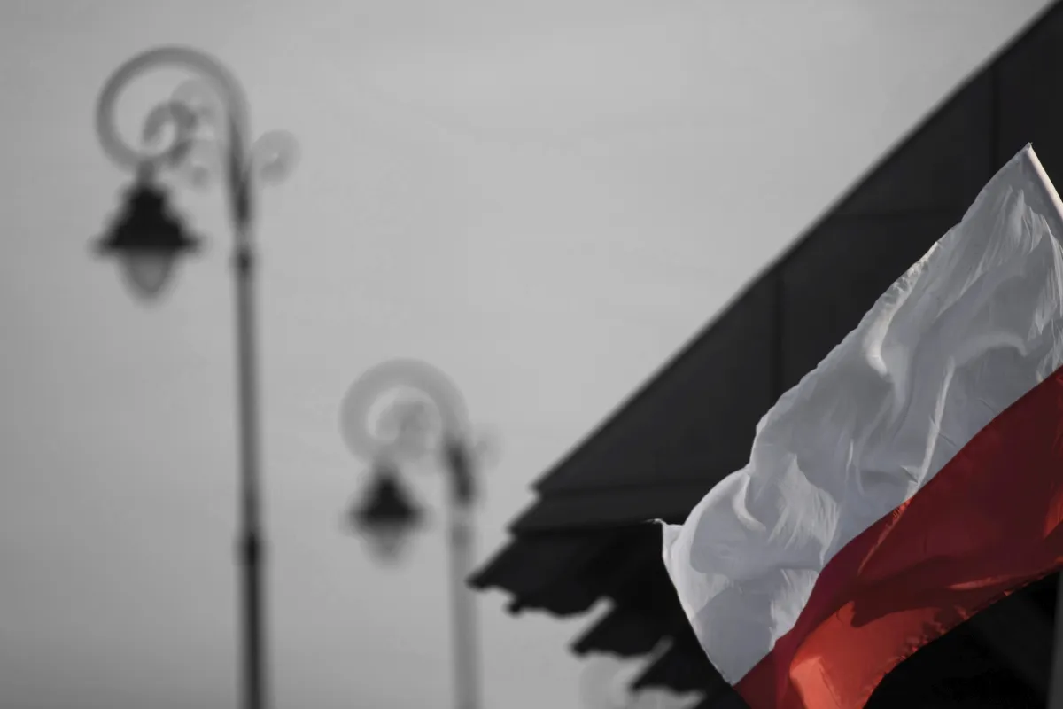 Polish flag beside blurred streetlamps and a rooftop edge